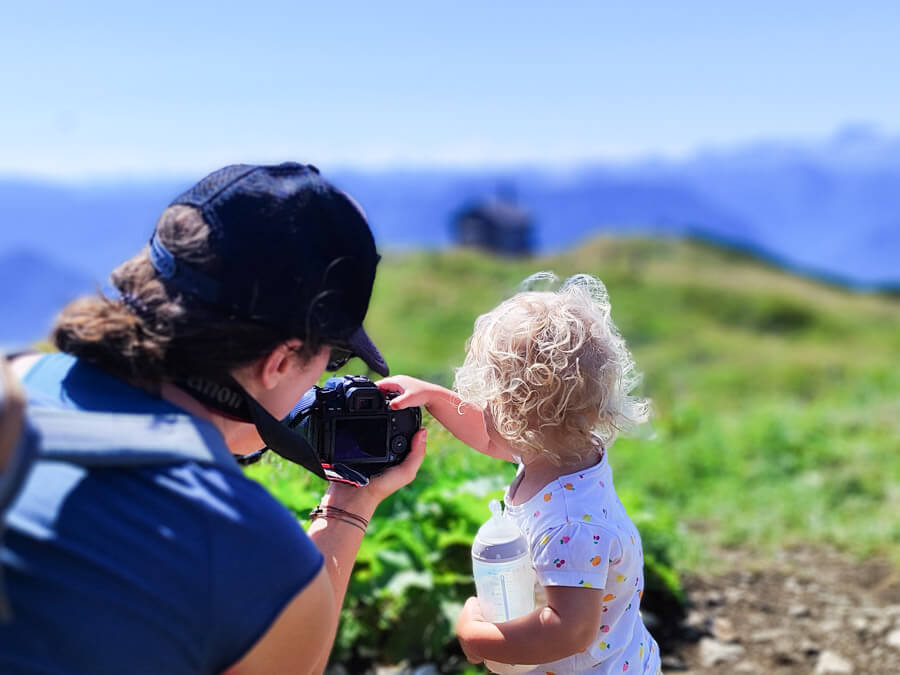 Familienfotografin mit Tochter beim gemeinsamen Wandern, die Tochter probiert sich an der Kamera aus