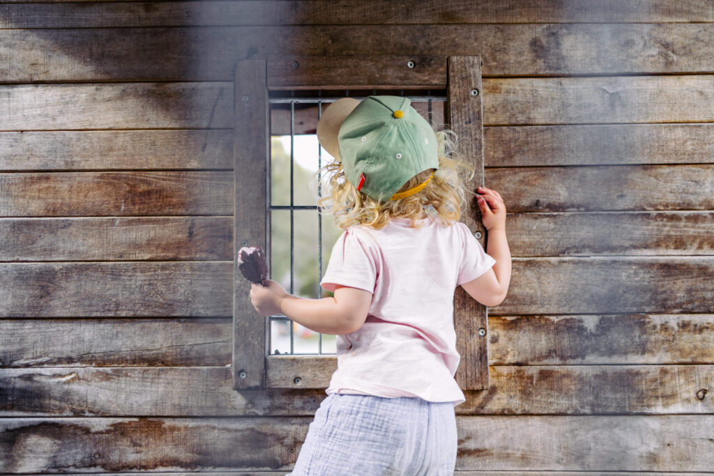 Kind mit Eis blickt aus Holzhaus bei Sommerausflug rund um Graz