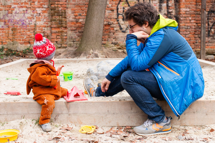 Kind sitzt mit Papa  in der Sandkiste